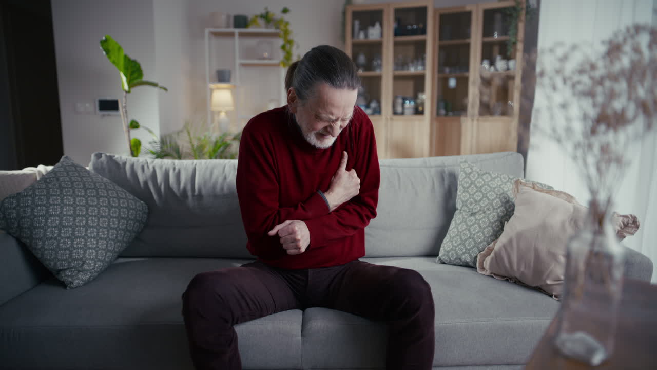 Elderly Man Experiencing Severe Chest Pain While Sitting on Couch at Home