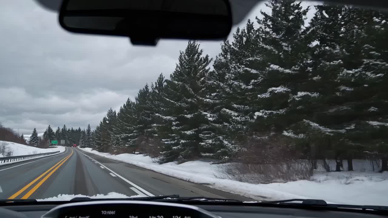 POV video from inside a car driving on a snowy road lined with pine trees