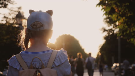 A-Girl-With-A-Backpack-Is-In-A-City-Park-Passersby-Go-By