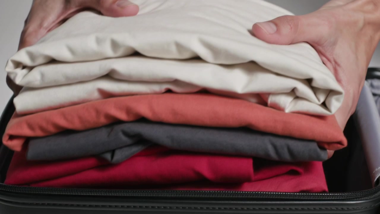 Reaching hands placing smoothing lifting folded clothes from zipped suitcase on table for packing