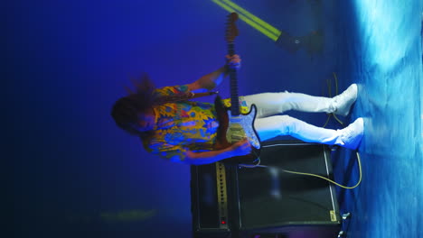 vertical video of a crazy jumping rock guitarist with a guitar in his hands on a colored neon background dancing and playing the guitar. concert light