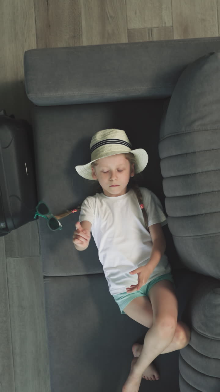 niño en edad preescolar aburrido juega con gafas de sol descansando en el sofá en la habitación del hotel. niña pequeña espera actividades en el balneario vacaciones vista superior