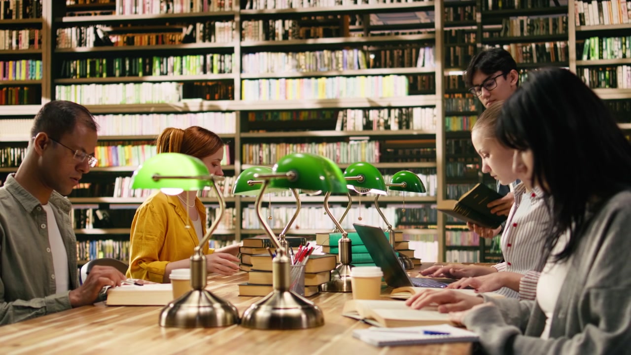 Studenti universitari si concentrano su libri e appunti a un lungo tavolo della biblioteca