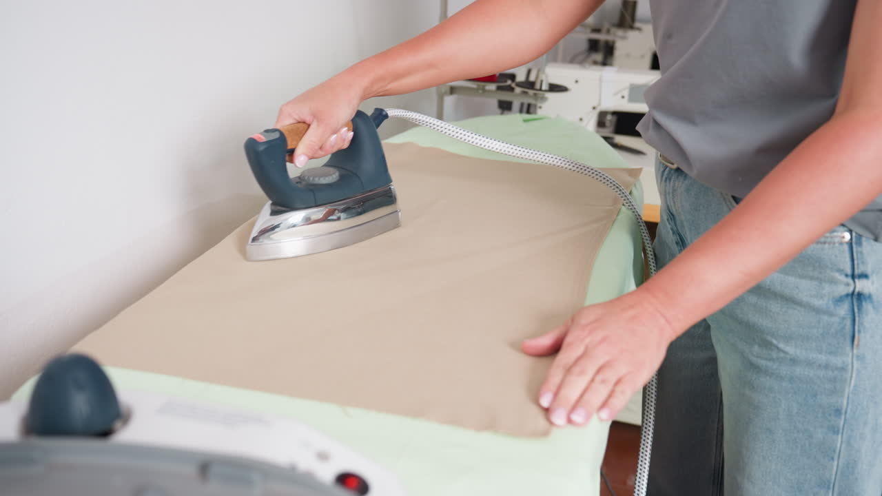 Steam iron straightening cloth on ironing board, smoothing wrinkles, producing crisp finish, demonstrating meticulous technique, focusing on careful pressing, ensuring neat appearance