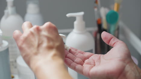 Practitioner presses pump tip to dispense clear massage cream onto hands, spreads cream evenly over palms and fingers before applying to visitor face, emphasizing smooth texture