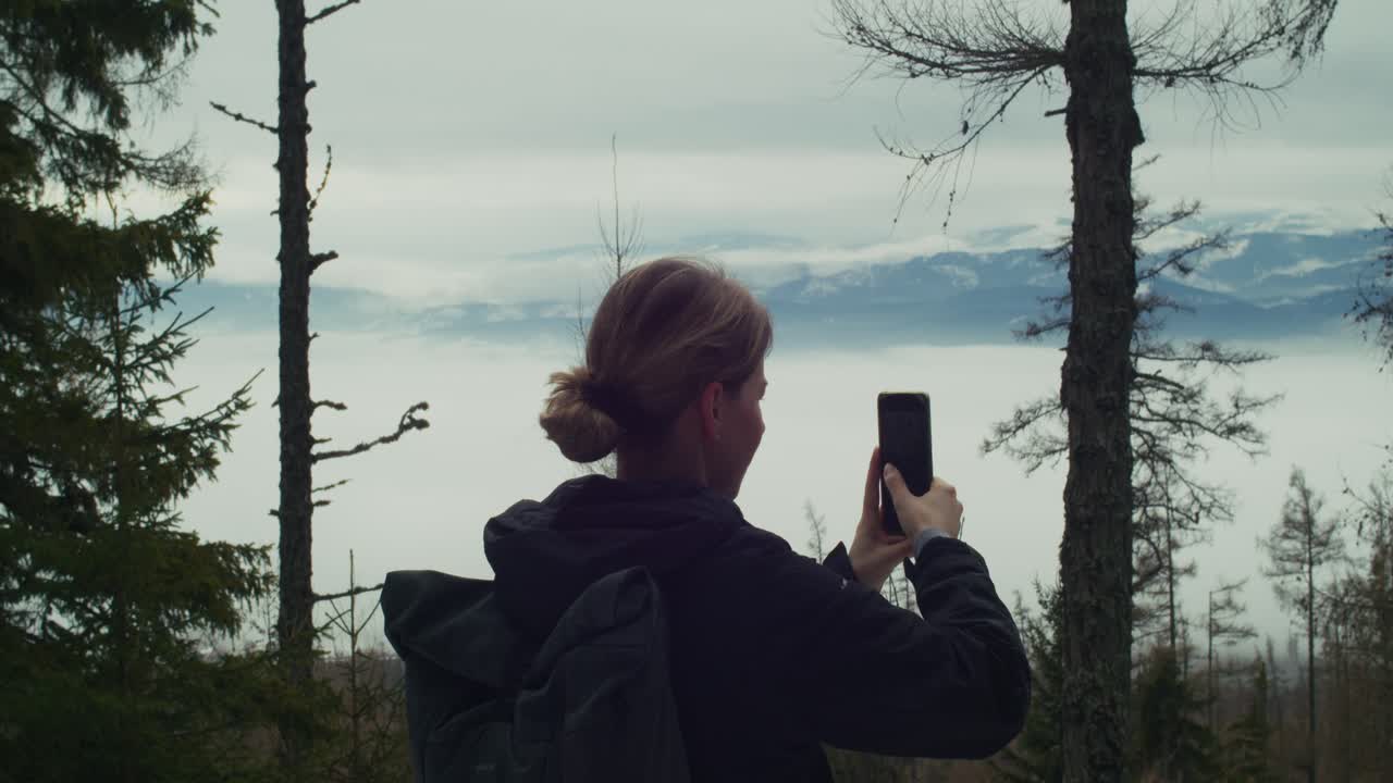 Woman taking photo of High Tatras mountains from forest viewpoint