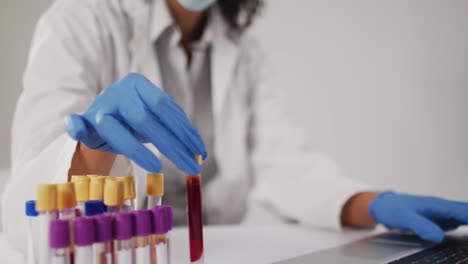 video of biracial female doctor holding test tube and using laptop on blue background