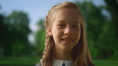 smiling blonde little girl posing alone in park closeup. romantic dreamy child