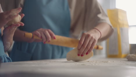 Ama-De-Casa-Está-Extendiendo-Masa-Con-Un-Rodillo-En-La-Cocina-La-Pequeña-Hija-Está-Ayudando-A-La-Madre