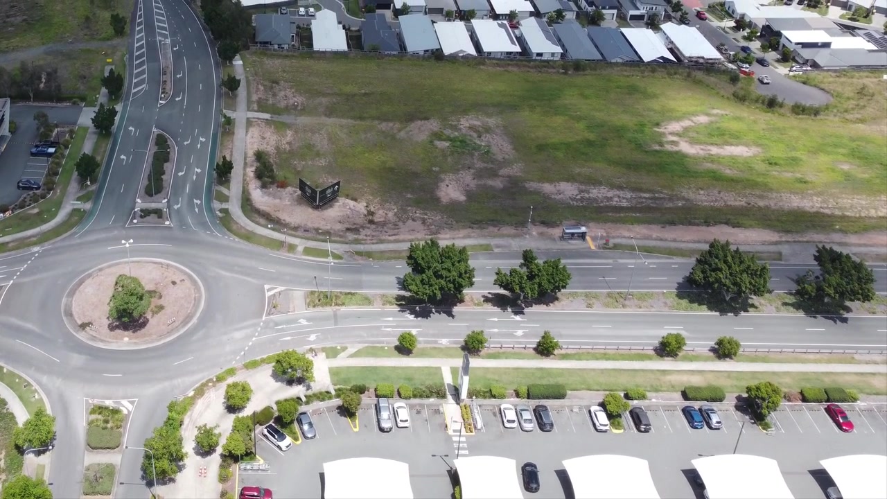 Sorvolando il parcheggio di un piccolo centro commerciale verso una rotonda e un quartiere residenziale in Australia.