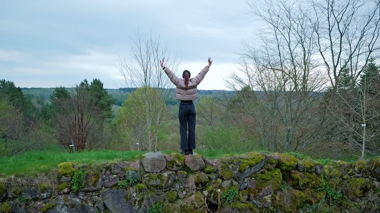 Slow motion shot of woman raising arms in freedom at Rucava hilltop