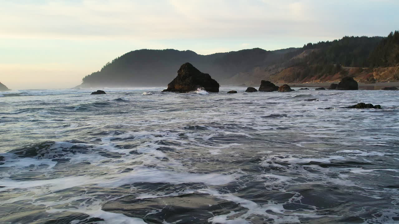 A drone shot going of the ocean with waves and sea stacks passing by