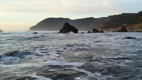 a drone shot going of the ocean with waves and sea stacks passing by