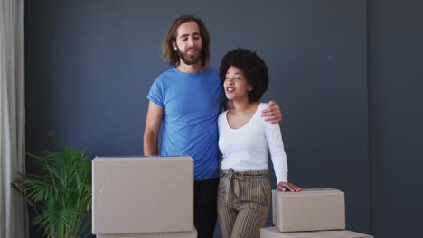 Mixed-race-couple-standing-in-between-cardboard-boxes-at-new-apartment-house