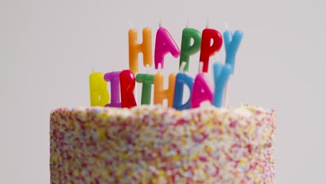 studio shot of revolving birthday cake covered with decorations and candles spelling out happy birthday 1