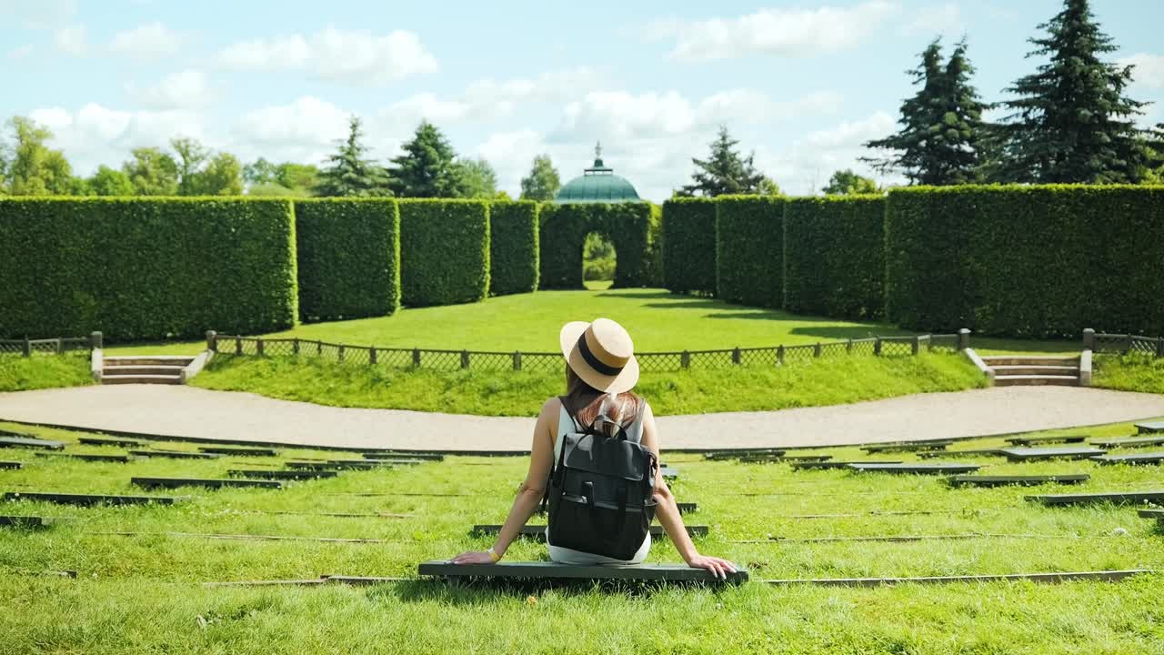 Vertical camera tilt, woman seated in symmetrical hedge amphitheatre scene