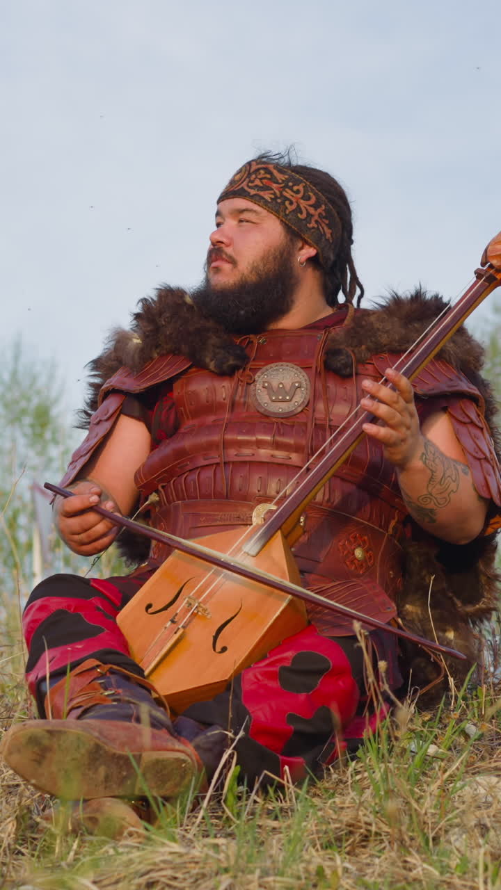 Dreaming man with overweight plays stringed instrument sitting on hill grass. Inspiring Siberian melodies. Open musical festival of Altai culture