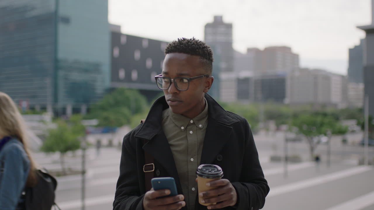 portrait of young trendy african american man student texting browsing social media using smartphone drinking coffee beverage in busy city people walking urban lifestyle