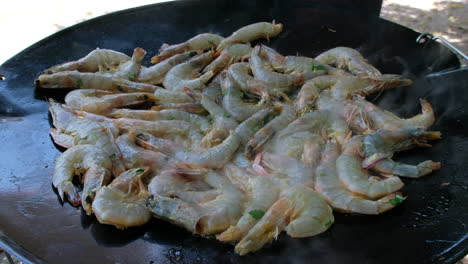 prawns and shrimps being cooked on an outdoor gas powered skottle pan and tossed in oil