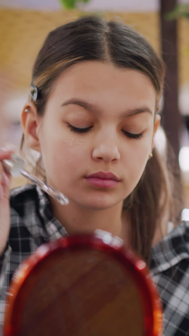 Cura della pelle per adolescenti, applicazione di siero a gocce, giovane donna che massaggia delicatamente il siero per il viso allo specchio, adolescente che esegue una routine di cura della pelle dettagliata in interni con illuminazione calda