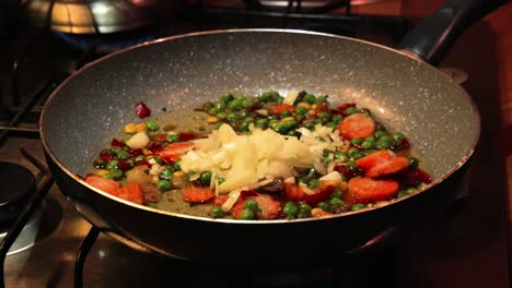 Pouring fresh chopped onions to a hot frying pan with vegetables in it