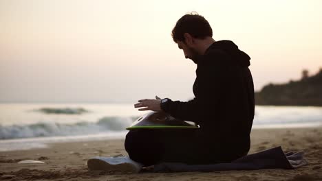 el hombre jugando a colgar sentado en la playa frente al mar solo