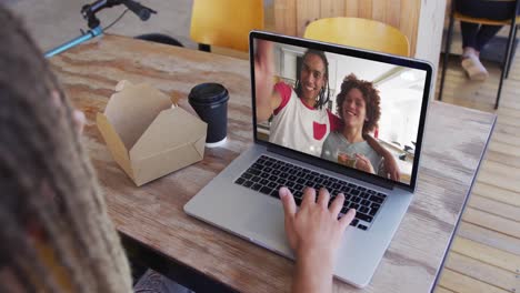 Woman-having-a-snack-while-having-a-video-call-on-laptop-at-a-cafe