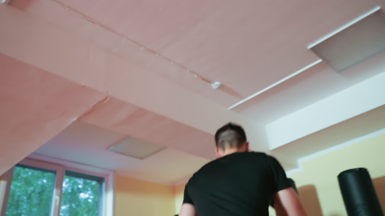 Grapplers engaged in sparring session inside gym with boxing gloves, showing fast motion and athletic intensity, training combat skills, focus, discipline, and endurance under ceiling lights near windows