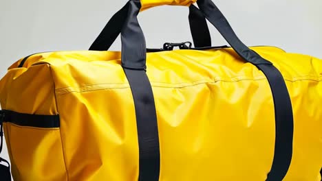 a yellow duffel bag with black straps on a white background