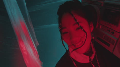 cheerful asian girl in 90s outfit holding boombox and dancing in neon light