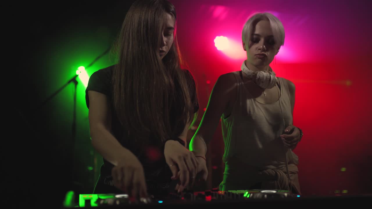 dos hermosas mujeres jóvenes dj tocan la música en la consola de mezcla en el club nocturno