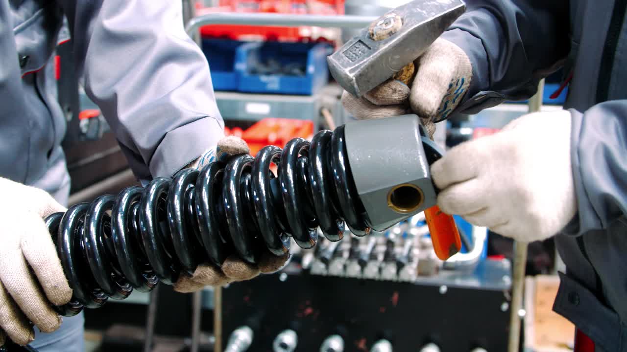 los trabajadores fijan el resorte negro durante el montaje del amortiguador en la planta industrial