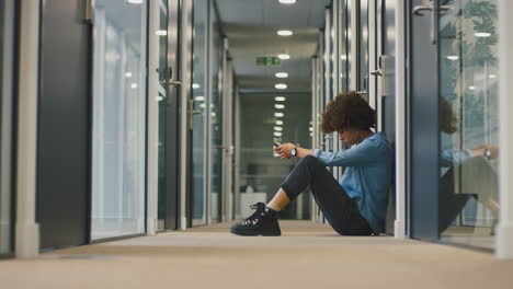 mujer de negocios joven estresada sentada en el piso en el corredor de una oficina moderna con teléfono