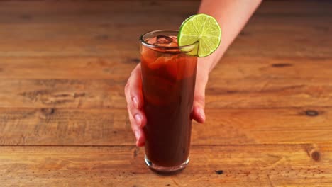 close up of a cuba libre cocktail being removed from a wooden table in a restaurant