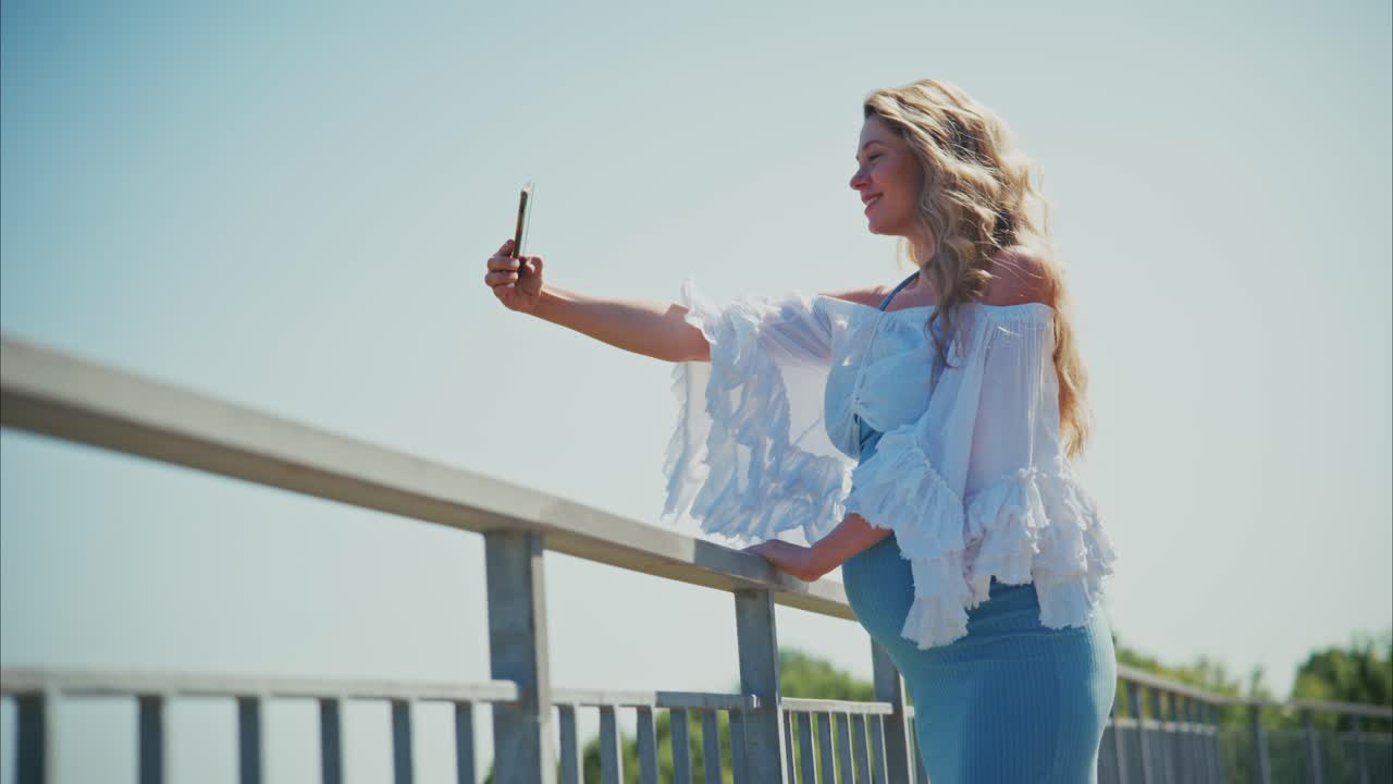 Glückliche Schwangere macht Selfie mit Smartphone im Freien