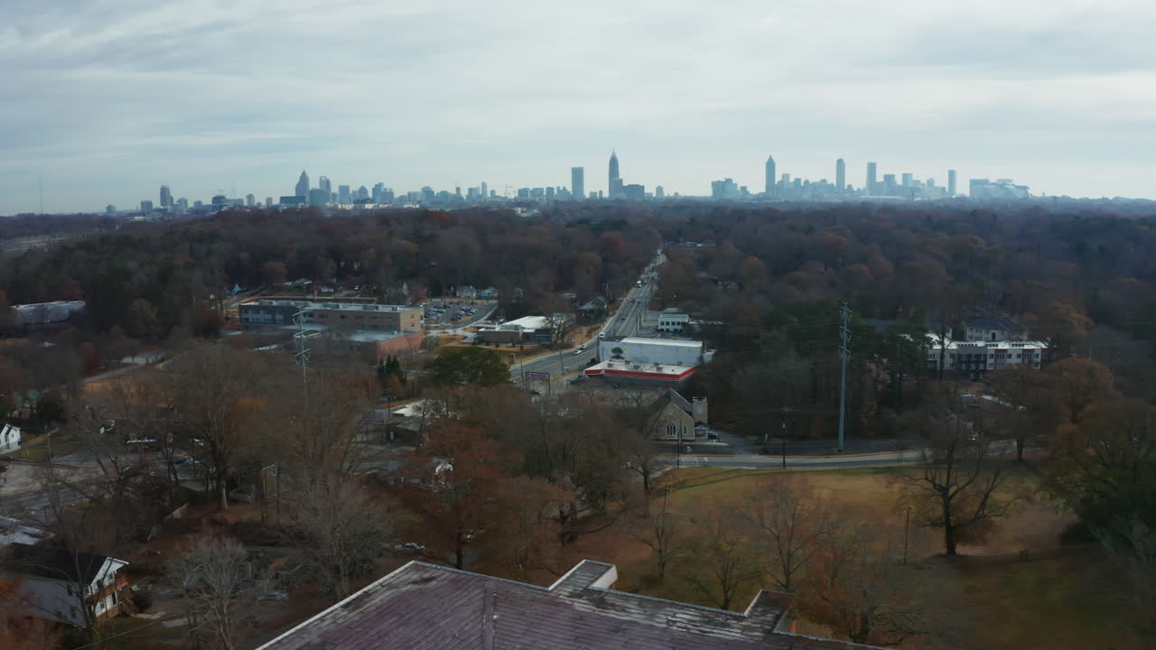 A scenic rotating aerial over the tree canopy surrounding the suburbs of Atlanta, with a busy road and drivers coming to and from the city, with the skyline in the background cityscape.