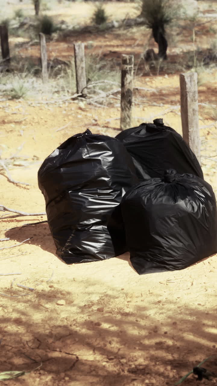 Trash bags left near a dirt road surrounded by dust and trees