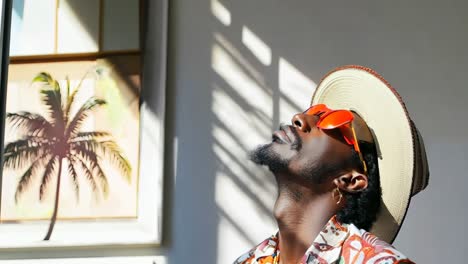 a man wearing a hat and sunglasses standing in front of a wall