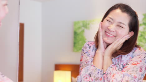 아름다운 아시아 여성이 욕실 거울을 바라보고 그녀의 울창한 검은 머리카락을 만지고, 그녀의 외모를 즐긴다.