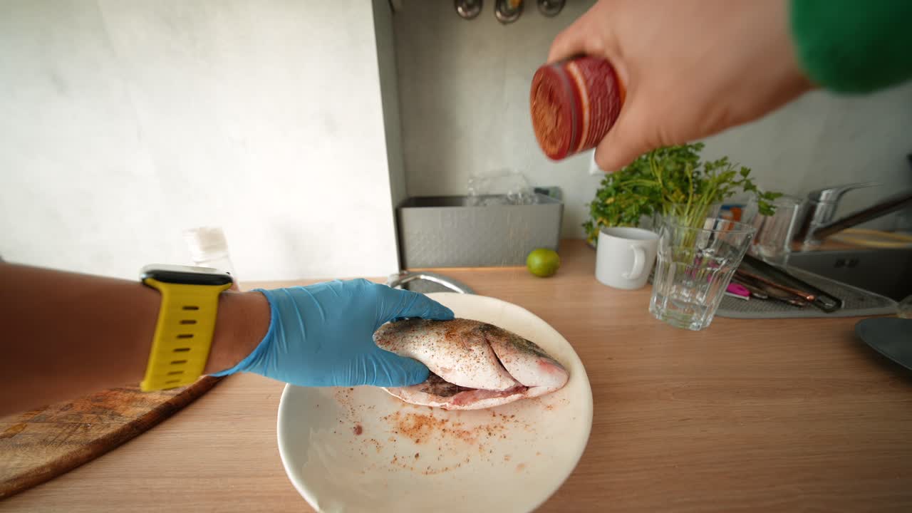 Manos sazonando pescado entero fresco en un plato en una cocina