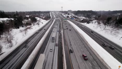 tracking aerial flyover of busy winter highway with blowing snow and transport trucks in scarborough toronto east 401, overcast day