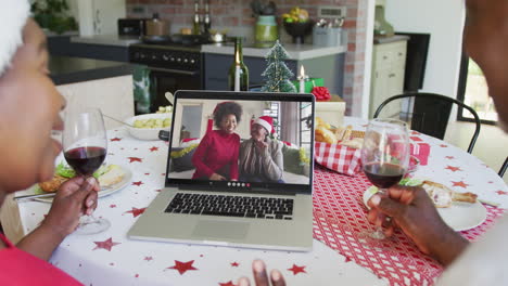 pareja afroamericana con vino usando computadora portátil para la videollamada de navidad con la familia en la pantalla