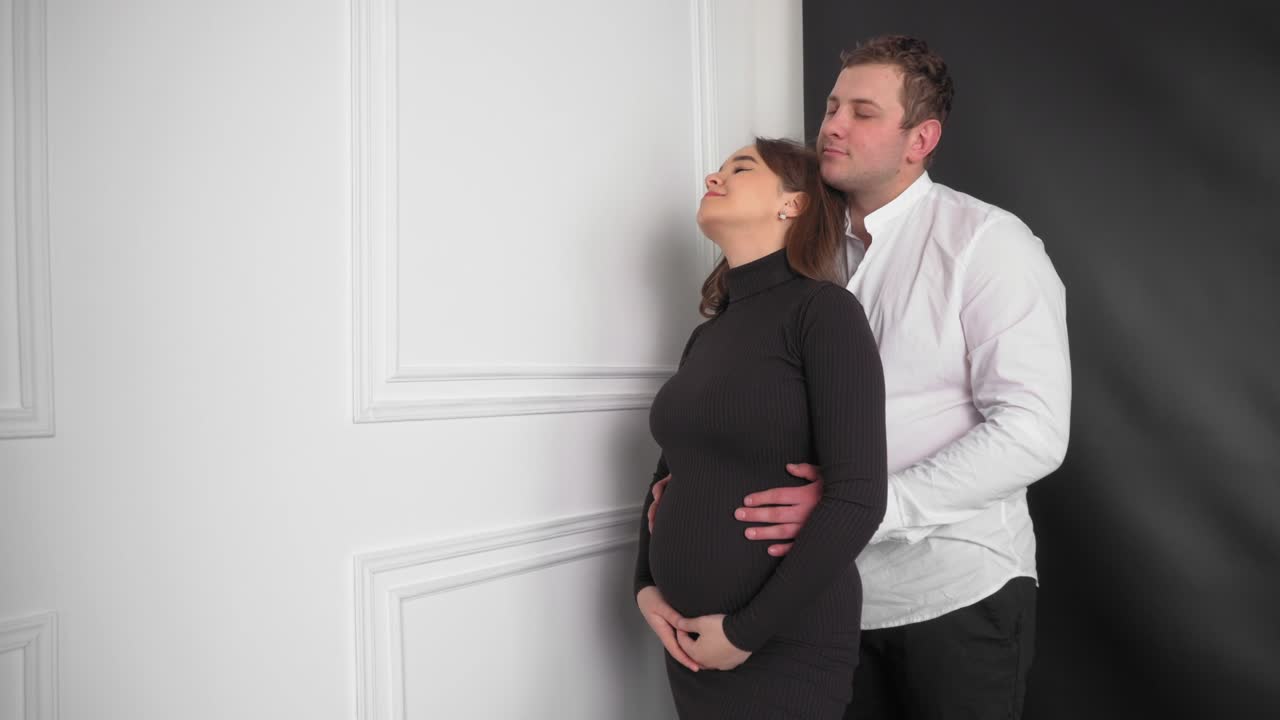 임신한 젊은 여성과 남편은 아기를 기대하고 있습니다. 젊은 가족은 보충을 기다리고 있습니다. 집에서 휴식을 취하는 큰 배를 가진 행복한 임신한 여성. 젊은 임신하는 어머니는 그녀의 배를 만져줍니다.