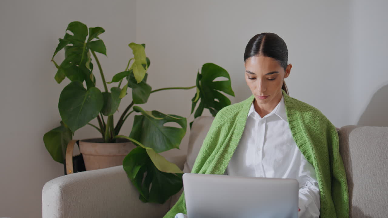 una mujer seria enviando mensajes de texto al ordenador en el sofá de cerca. una estudiante que aprende a distancia.