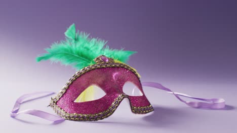 video of pink carnival masquerade mask with green feathers on white and purple background