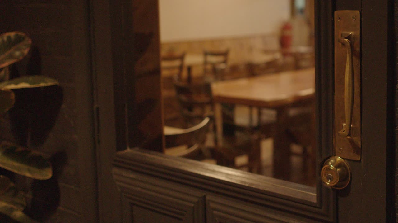 Hand opens glass door, enters warmly lit empty restaurant, camera follows with smooth movement inside