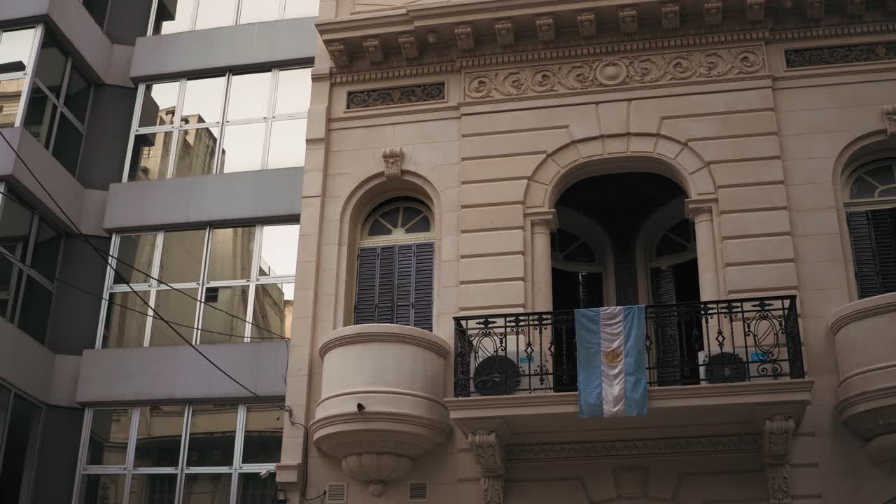 bandera argentina colgando del balcón de una casa de estilo neoclásico