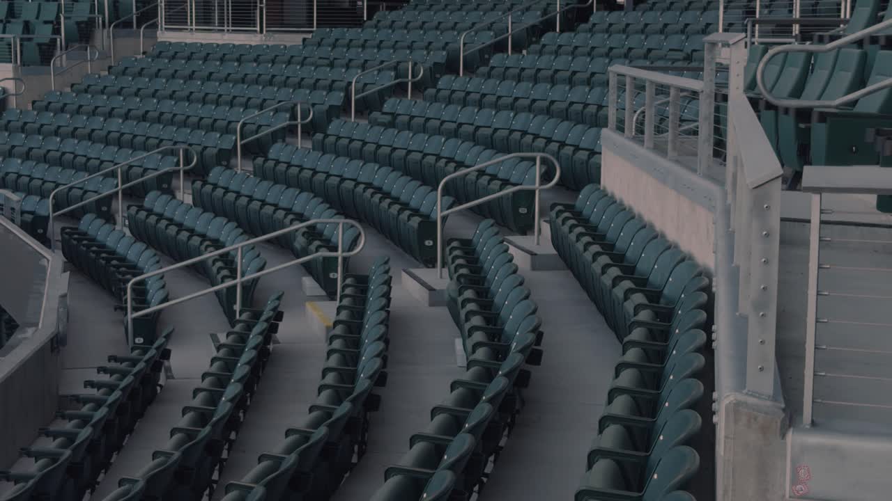 Langsom, jævn panorering fra højre mod venstre over tomme stadionsæder, rækværk og buede gange.