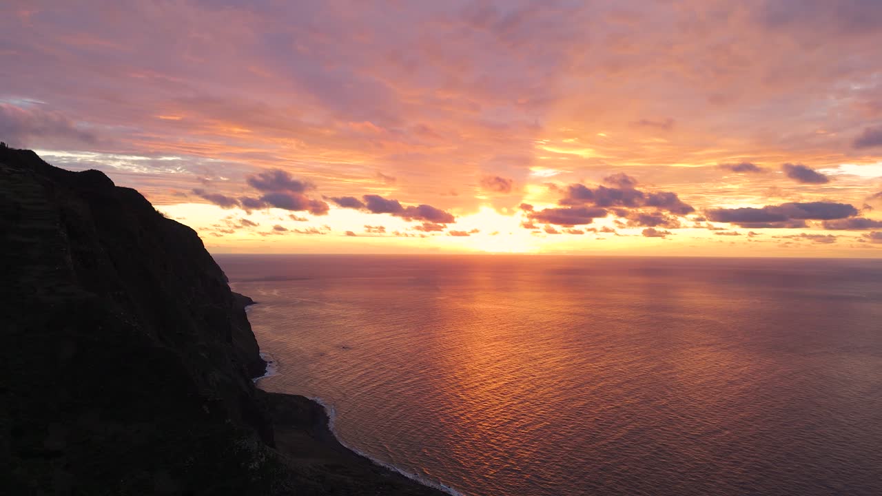 Breathtaking reveal shot during golden sunset at Ponta da Ladeira cliffs of Madeira, spectacular coastline stretching into the horizon lit by bright glowing evening sun