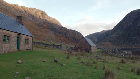 a slow right pan reveals multiple abandoned old stone buildings and a scottish bothy called glendhu set amongst steep cliff, mountains and a sea loch in a remote glen in rural scotland